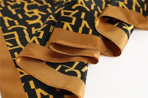 Detailed view of luxury black and gold silk scarf featuring satin sheen and letter patterns