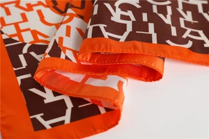 Close-up of luxury silk-like scarf with orange borders and geometric letter pattern