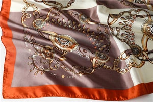 Detailed close-up of silk-like satin scarf with orange borders and horse-bit chain patterns