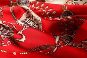 Detail of red satin scarf featuring elegant chain, buckle, and stirrup equestrian patterns
