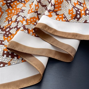 Macro detail of silk scarf featuring orange and brown H-letter patterns and fine rolled edges