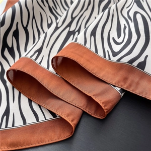 Detailed macro view of zebra pattern silk scarf with burnt orange edges and glossy texture