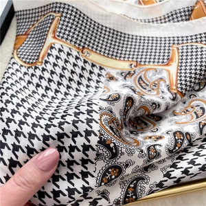 Close-up of retro silk scarf featuring black houndstooth and orange horsebit patterns