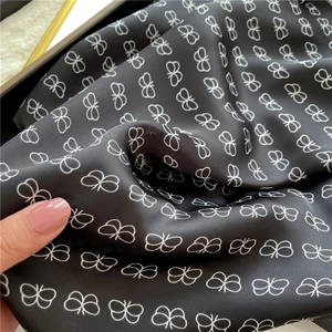 Detail showing high-quality black satin scarf texture with white butterfly patterns