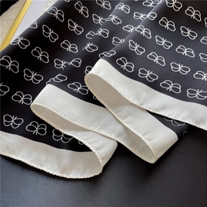 Close-up of elegant black silk scarf with white butterfly print and smooth texture