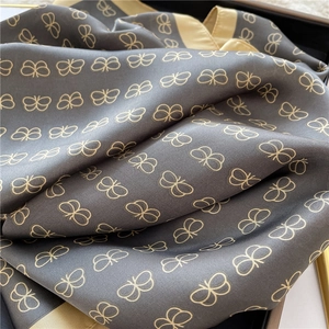 Detailed view of dark grey silk scarf with golden butterfly patterns and satin finish