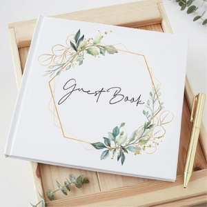 Elegant white guest book with gold geometric frames and floral greenery for weddings