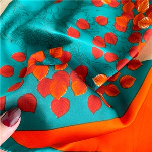 Detailed macro shot of silky teal scarf with vibrant red leaf patterns and orange borders