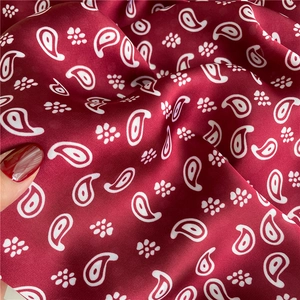 Macro detail of wine red silk scarf featuring white paisley pattern and smooth satin texture
