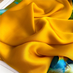 Detailed close-up showing glossy yellow silk fabric texture with blue-green artistic print