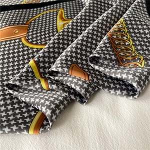 Detail of luxury silk scarf showing golden horsebit chains over classic black houndstooth