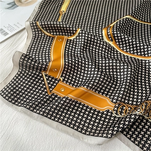 Close-up of silk scarf with houndstooth pattern and luxury buckle print on white fabric