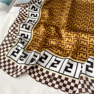 Close-up of silk scarf with brown and white monogram pattern and checkered border texture