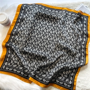 Détail d'un foulard en soie de luxe avec motif cachemire noir et blanc et bordure orange