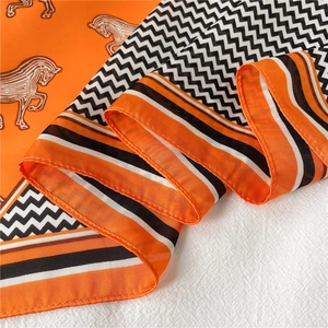 Dettaglio di un foulard in seta con motivo a cavallo arancio e nero e trama a spina