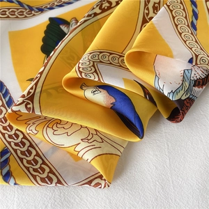 Detail van een gele zijden sjaal met klassieke kettingprints en illustraties van vogels