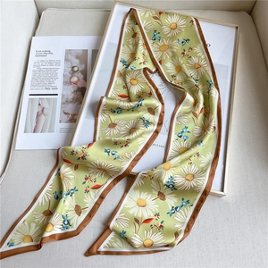 Détail d'un foulard twilly vert avec motif marguerite et bordure marron sur magazine