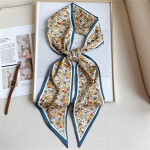 Détail d'un foulard étroit en soie à motif floral avec bordure bleue sur tissu beige