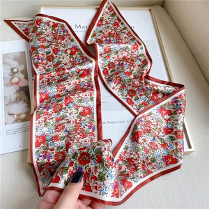 Détail d'un foulard étroit en soie fleurie multicolore avec bordure rouge sur tissu beige