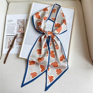 Détail d'un foulard étroit beige à fleurs noué en boucle sur un cadre blanc