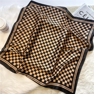 Classic black and gold checkered silk square scarf displayed on white plush rug