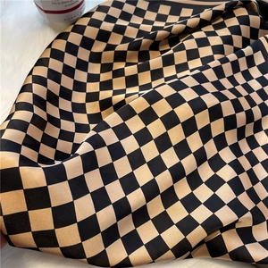 Detailed view of black and gold checkerboard silk-like scarf on soft plush background
