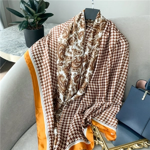 Detail of silk-like scarf with paisley and houndstooth patterns on a grey sofa