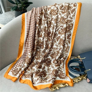 Retro houndstooth paisley silk scarf with orange border draped on a grey sofa