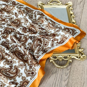 Detailed texture of paisley print silk scarf with bright orange borders on wooden background