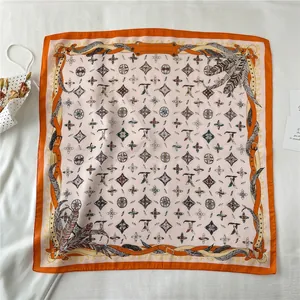 Detailed close-up of orange silk scarf with luxury monogram and feather motifs