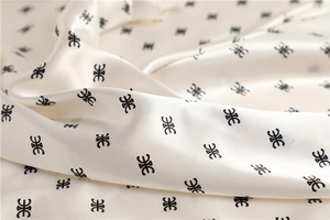 Dettaglio macro di un foulard in raso crema con pieghe morbide e motivi logati geometrici