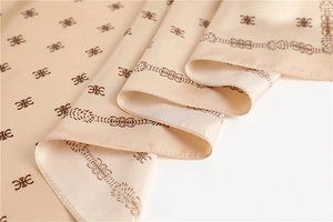 Dettaglio macro del foulard di seta champagne con motivo monogramma vintage a pieghe