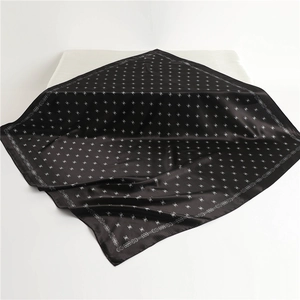 Foulard quadrato in raso nero con motivi bianchi esposto su un piedistallo bianco