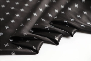 Vista macro di foulard in raso nero setoso con motivo monogramma argento e pieghe morbide