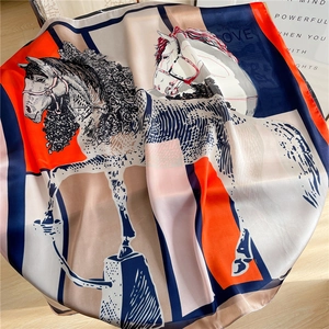 Detail of silk square scarf featuring orange and navy horse patterns with rolled edges