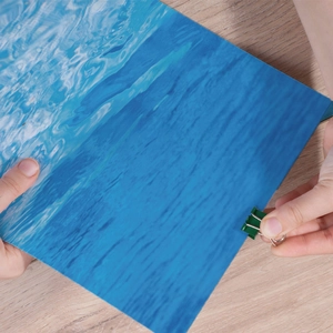 Blue ocean wave pattern scrapbooking paper for DIY crafts held on a wooden table