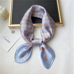 Élégant foulard en soie à damier bleu clair et bronze, noué avec style sur socle en pierre