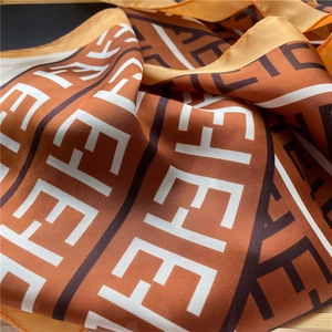Detailed macro view of orange and brown geometric letter silk scarf on bamboo background