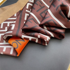 Detailed close-up of striped silk-like scarf featuring geometric monogram pattern