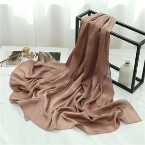 Detail of caramel silk scarf with accordion pleats hanging on a minimalist black frame