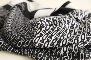 Detail shot of black and white silk scarf with luxury chain and letter patterns