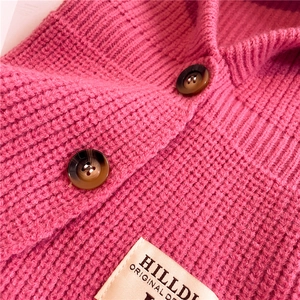 Dettaglio della maglia spessa rosso rosa con bottoni ambra ed etichetta del marchio sciarpa
