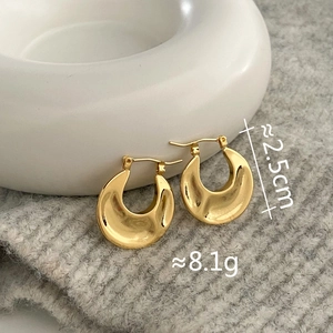 Detail of 2.5cm chunky gold hoop earrings with polished finish on a soft fabric backdrop