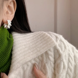 Detail of matte gold irregular pleated hoop earrings on model with green sweater