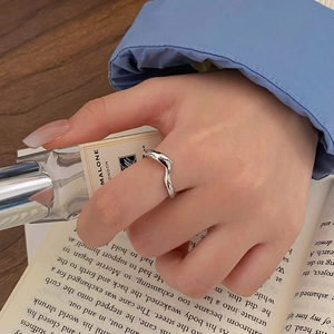 Close-up of minimalist silver wave ring on a hand with aesthetic lifestyle props