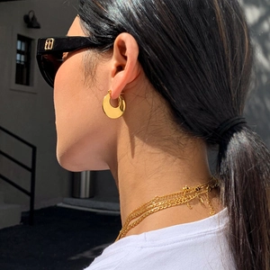 Close-up of golden chunky C-shaped hoop earrings on model under bright sunlight