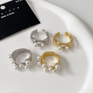 Eleganti anelli coreani in oro e argento con perle in un piatto di ceramica bianca