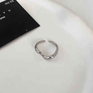 Detail of silver wavy open ring with high-polished finish on a white ceramic plate