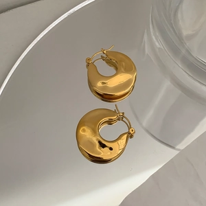 Macro reflection of gold-plated chunky hoop earrings on a sleek silver mirror surface