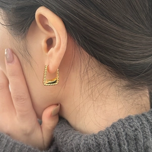 Close-up of gold geometric square earrings with beaded texture on a knit sweater background